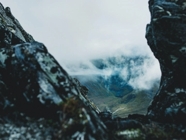 Fotografi med utsikt utover en fjelldal, tatt mellom fjellknauser i forgrunnen